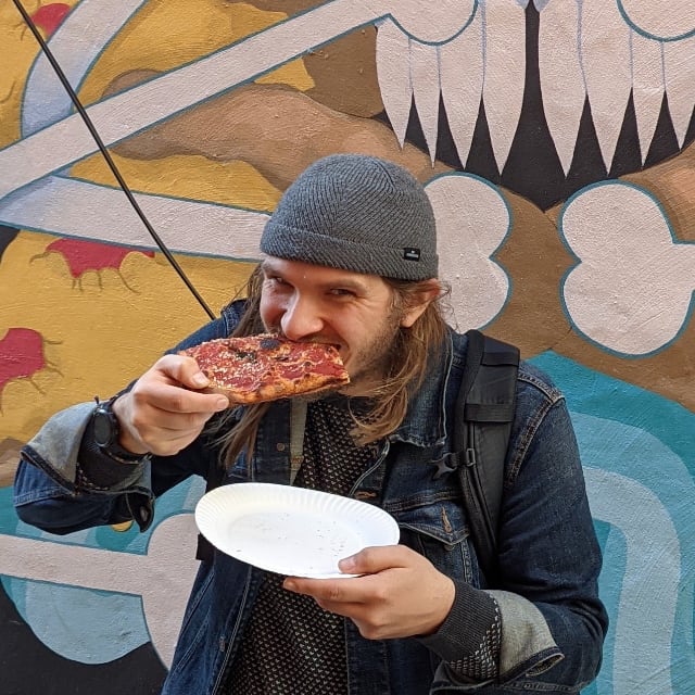 Photo of Brett Chalupa eating a slice of vegan pizza